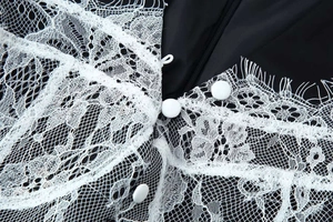 Detailed close-up of white eyelash lace embroidery and round buttons on a black dress