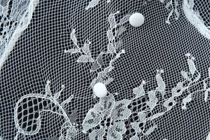 Detail shot of white lace dress with floral patterns and round fabric buttons