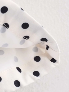 Detailed close-up of double-stitched hem on white polka dot long sleeve jacket fabric