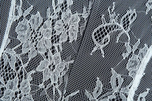 Macro shot of intricate white floral lace detailing and mesh texture on the dress