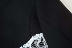 Close-up detail of delicate white lace stitching on black fabric with fine mesh texture