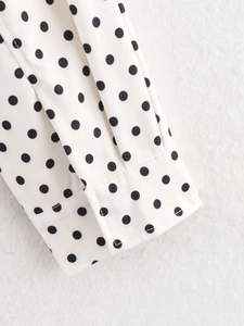Detail of polka dot long sleeve cuff with button closure on off-white woven fabric