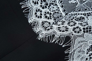 Detail of elegant black fabric with intricate white floral eyelash lace trim and stitching