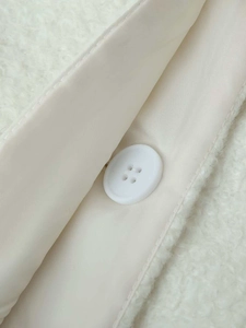 Detail of soft cream white sherpa fleece fabric with matching button and smooth lining