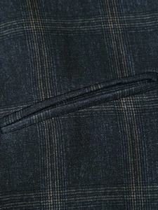 Detailed close-up of dark blue plaid fabric with single-welt pocket and precise stitching