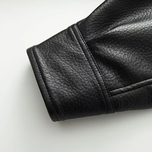 Detail of black faux leather jacket cuff featuring pebble grain texture and fine stitching