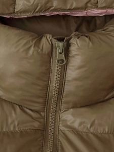 Detail of olive green puffer jacket featuring pink contrast lining and metal zipper