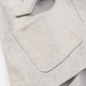 Detailed close-up of wool texture and precise stitching on the grey poncho coat pocket