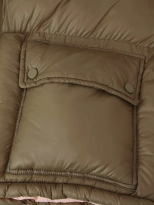 Detailed macro view of olive-brown padded jacket with quilted texture and snap-button pocket