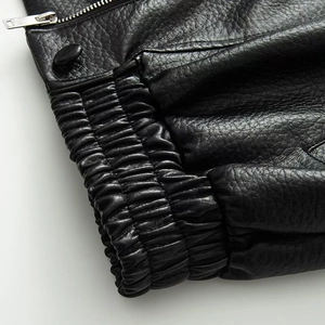 Detail of black faux leather jacket featuring elastic cuffs and a silver metal zipper
