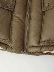 Detail of dark brown puffer jacket featuring flap pockets and bright pink lining contrast