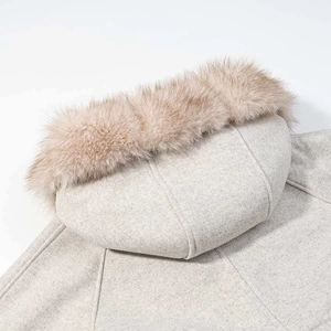 Close-up of the beige wool cape coat featuring a fluffy faux fur trim on the hood