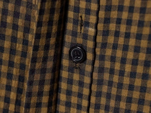 Detailed close-up of the black resin button and brown checkered fabric on the shirt