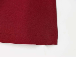 Close-up of red satin dress hem showing fine plain weave texture and neat stitching details