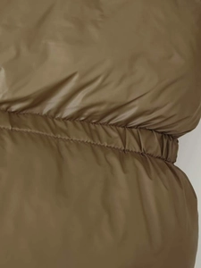 Detailed view of olive green quilted jacket featuring elastic gathered waist and stitching
