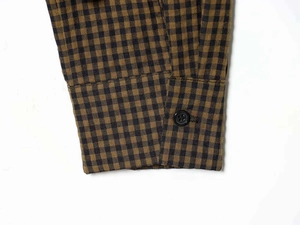Detail of sleeve cuff with black matte button on brown and black plaid shirt