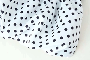 Detail of V-neck summer dress fabric featuring classic black polka dots on white background