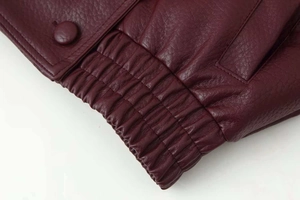 Gros plan sur la veste en cuir bordeaux avec ourlet élastique et bouton gainé assorti