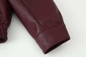 Détail macro de la veste en cuir bordeaux montrant le poignet et la texture de l'ourlet