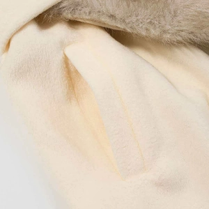 Detail of soft cream wool coat featuring a faux fur collar and a neat welt pocket