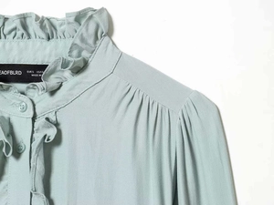 Detail of mint green ruffle collar blouse with button-up front and pleated design