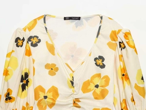Close-up of cream floral blouse with V-neck, pleated details and long puff sleeves