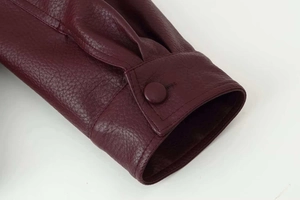 Gros plan du poignet d'une veste en cuir bordeaux montrant le grain de litchi et le bouton