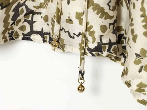 Détail d'une robe fleurie en lin avec motifs olive et embouts de cordon en métal doré
