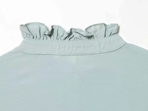 Detail shot of ruffles stand collar on a light grey-green shirt with fine stitching