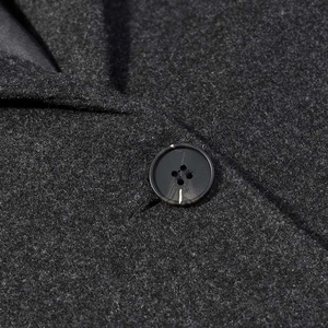 Detailed view of deep grey wool coat fabric with a classic four-hole resin button