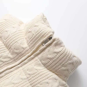 Close-up of the metal zipper and chunky cable knit texture on a beige vest collar