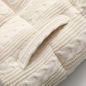 Close-up of cream white cable-knit texture and fine stitching on a warm knitted vest