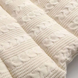 Macro shot of cream cable-knit pattern and thick quilted texture on knit vest jacket