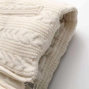 Close-up of cream cable knit vest texture showing the silver metal zipper detail