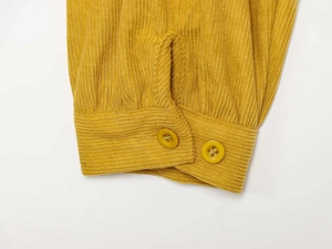Detail of yellow corduroy sleeve featuring parallel resin buttons and ribbed fabric texture