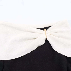 Detail of off-shoulder knitwear with white draped neckline and gold sphere pin fastener