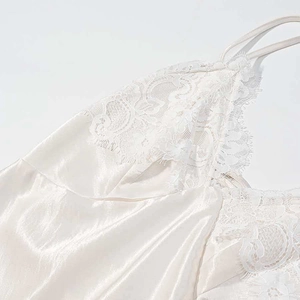 Detail of elegant beige satin slip dress featuring delicate white floral lace and eyelash trim
