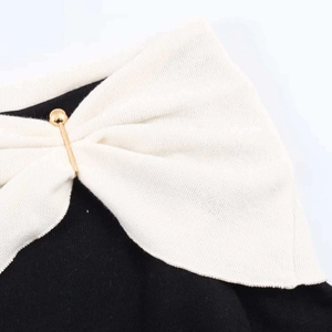 Detail of black knit sweater with cream bow neckline and decorative gold metal pin