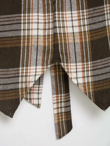 Detail of asymmetrical hem and side tie on a brown plaid shirt with twill texture
