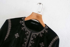 Détail de veste en velours noir avec broderie géométrique dorée et sequins au col