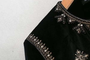 Détail de broderie en fil doré et paillettes sur veste en velours noir à col rond