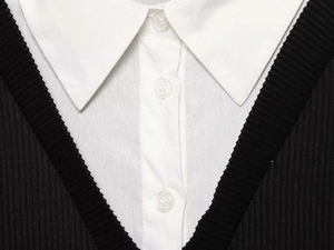 Detail of white poplin shirt collar with black V-neck knit overlay and resin buttons
