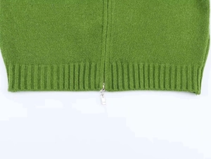 Detail of soft grass green knit cardigan with silver double zipper and ribbed hem texture