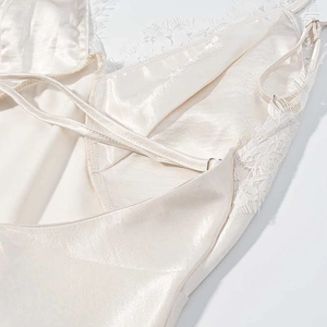 Detail of champagne satin slip dress featuring fine white lace and adjustable cross straps