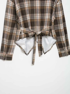 Detail view of the lace-up bow back and asymmetrical hem on a brown plaid shirt