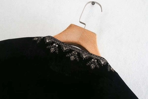 Détail macro de broderie dorée et sequins sur col en velours noir avec cintre en bois