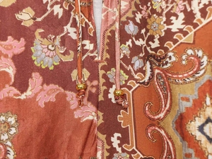 Dettaglio dello scollo a V su camicia con stampa paisley, coulisse e perle in metallo