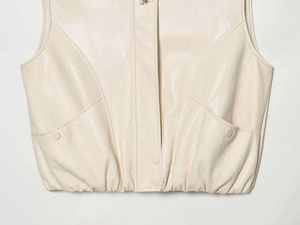 Detail of matte cream faux leather vest featuring snap buttons and elastic hem design