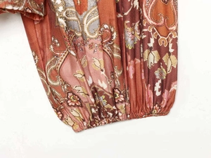 Dettaglio dei polsini elasticizzati e motivi paisley arancioni su una camicia boho
