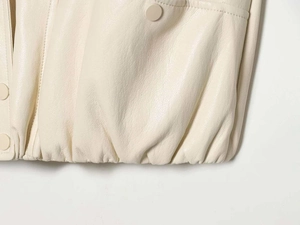 Detailed close-up of cream matte leather vest hem with fine stitching and matching button